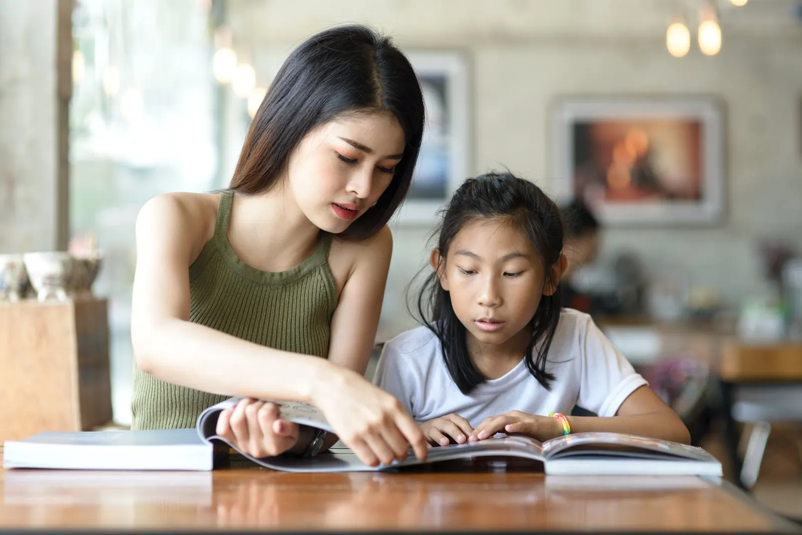 英語の本を指でたどりながら、娘の音読を見る母親