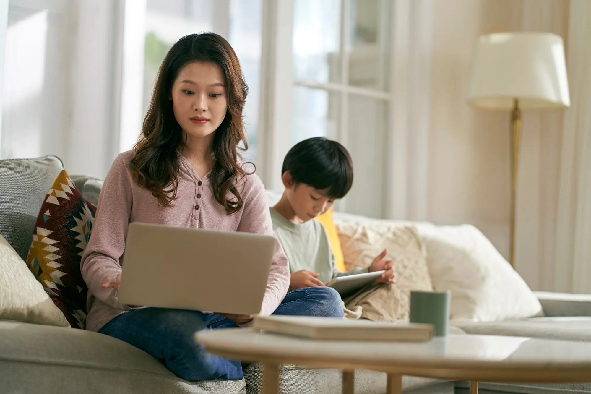ソファでノートパソコンを開く母親と、隣で本を読む息子