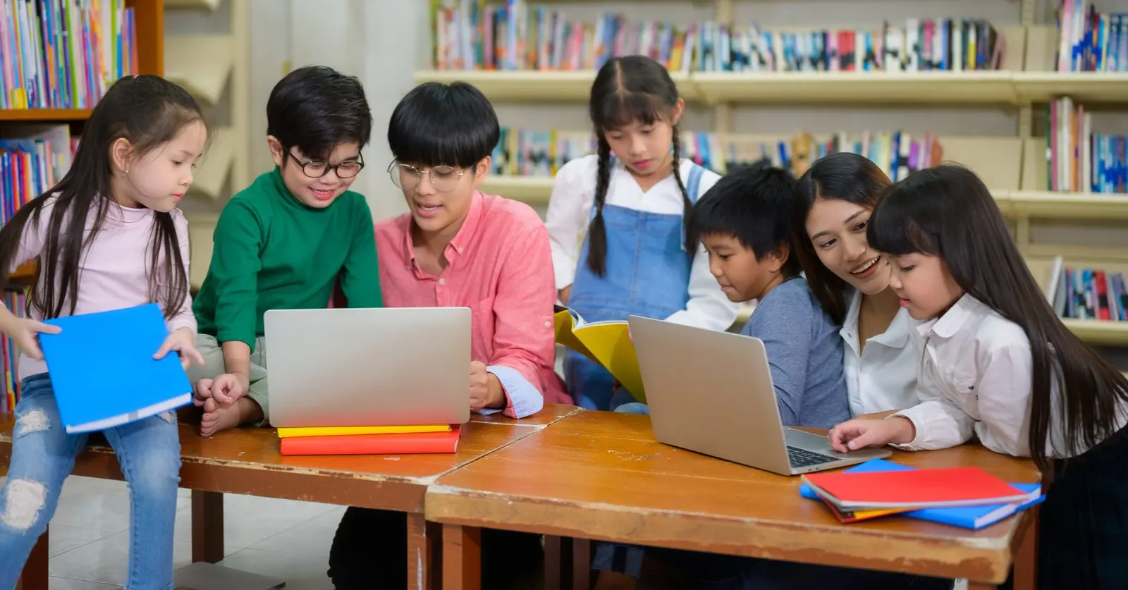 学校の図書室で、ノートパソコンや本を広げて学ぶ子どもたち