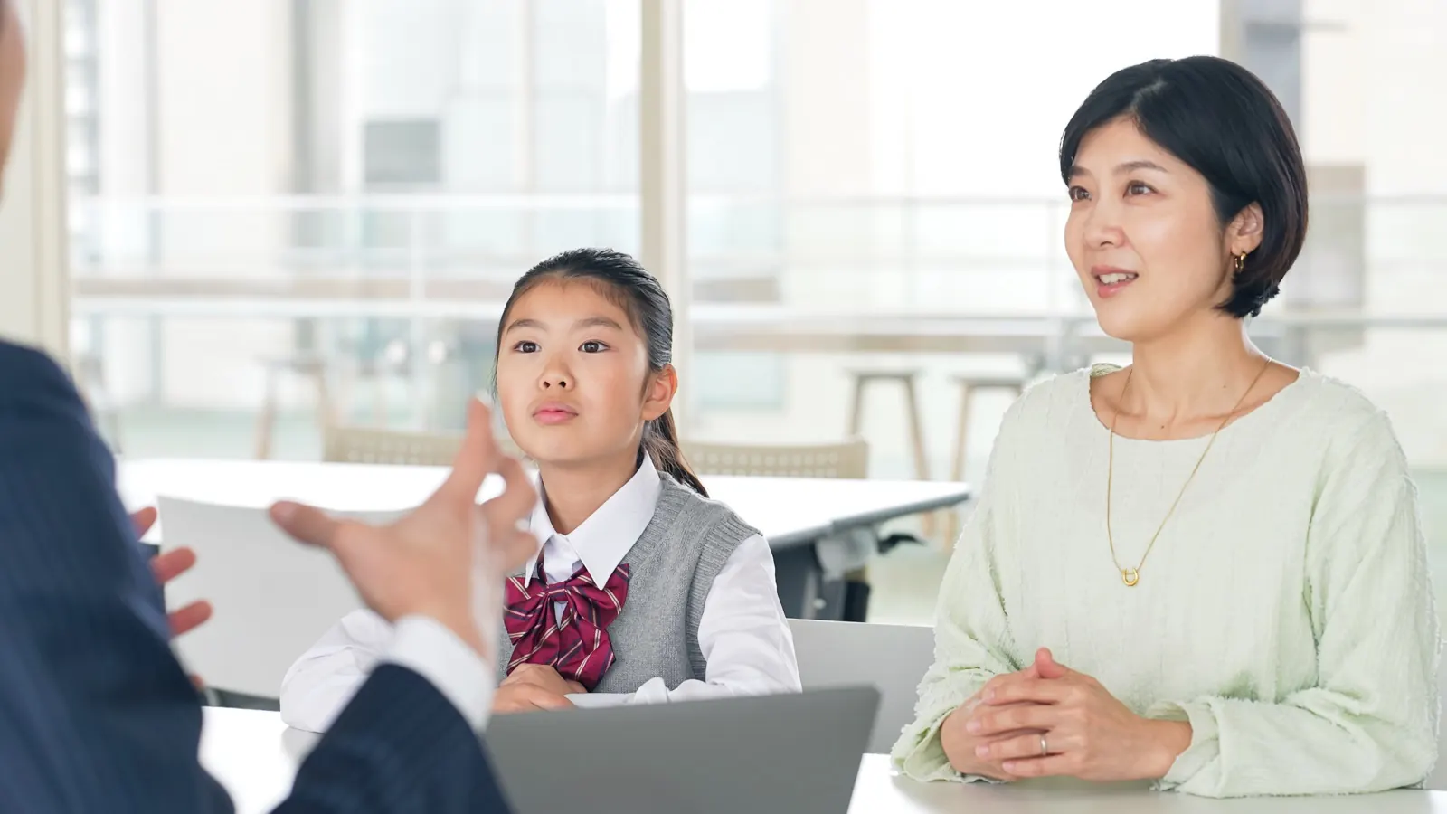 学校の一室で職員の説明を聞く母親と制服姿の娘