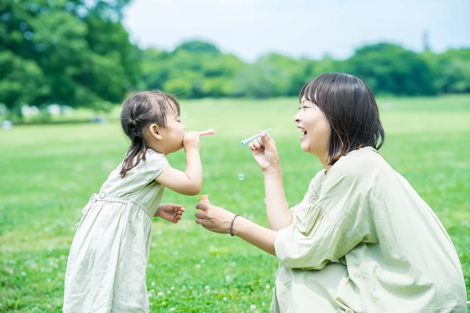 緑の芝生でシャボン玉を吹く娘と、しゃがんで見守る母親